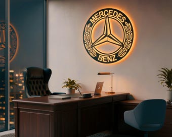 May include: An office interior with a large, illuminated Mercedes-Benz logo on the wall. The logo is black with a gold outline. A dark wood desk, a black leather chair, and a laptop are also present in the room.
