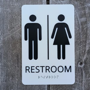 Letrero para baño que cumple con la ADA: Letras en relieve y braille, para todos los géneros, 6 x 9 pulgadas