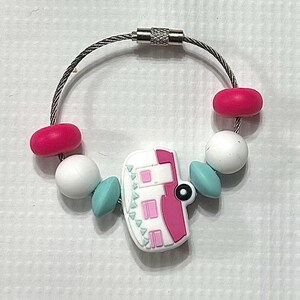 May include: A keychain with a silver wire loop and a white and pink camper charm. The keychain also features pink, white, and teal beads. The camper charm has windows and a door.