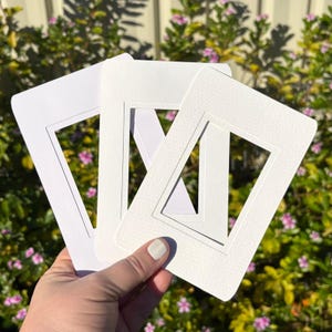 May include: Three rectangular white paper photo mounts with bevelled inner edges. Each mount features a clean, minimalist design with a smooth surface texture, designed to frame photographs or artwork with a crisp, professional white border.