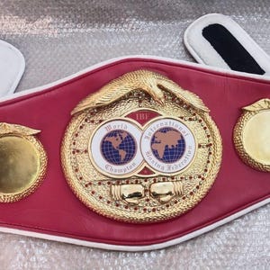 Pu&ograve; includere: Una cintura da campionato di boxe rossa e oro. La cintura presenta un grande emblema centrale con la scritta "World Champion" e "International Boxing Federation". Due emblemi dorati pi&ugrave; piccoli sono su entrambi i lati dell'emblema centrale.