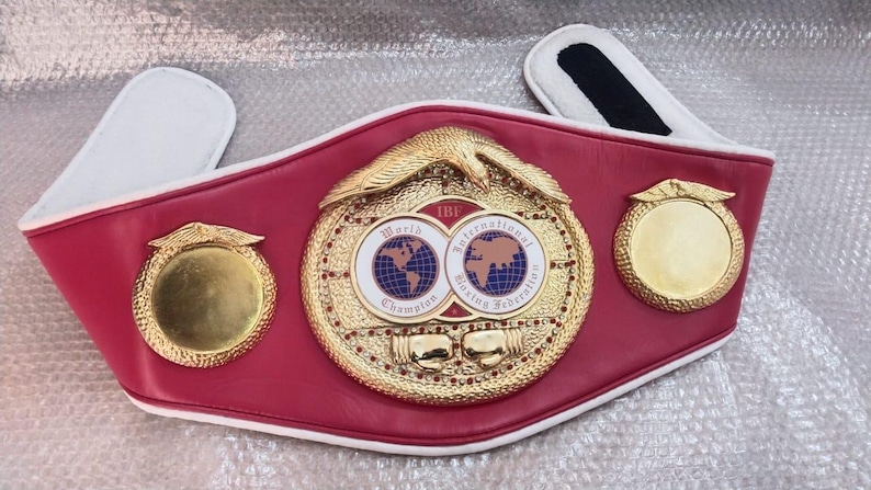 Pu&ograve; includere: Una cintura da campionato di boxe rossa e oro. La cintura presenta un grande emblema centrale con la scritta "World Champion" e "International Boxing Federation". Due emblemi dorati pi&ugrave; piccoli sono su entrambi i lati dell'emblema centrale.