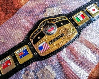 Può includere: Una cintura da campionato di wrestling in pelle nera con placche metalliche color oro. La cintura presenta la scritta "WORLDS HEAVYWEIGHT CHAMPION" e "WRESTLING". Include le bandiere di USA, Canada, Australia, Messico e Giappone.