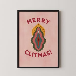 Op de afbeelding: Een ingelijste kunstdruk met een roze achtergrond en een gestileerde illustratie. De illustratie toont een gelaagd, kleurrijk ontwerp dat lijkt op een vulva, met de woorden "MERRY CLITMAS!" in rode letters erboven en eronder.