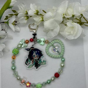 May include: A green and white beaded charm bracelet with a heart charm, a green and white character charm, and a variety of other charms, including stars, flowers, and bows.