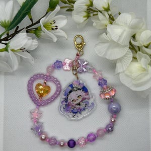 May include: A purple and pink beaded charm bracelet with a heart-shaped charm, a star-shaped charm, and a charm featuring a cartoon character. The bracelet has a gold clasp and is decorated with small pink and purple beads.