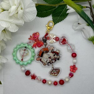 Puede incluir: Un brazalete de abalorios rojo, blanco y verde con un abalorio en forma de corazón, un abalorio de personaje y un pequeño abalorio de caja de regalo. El brazalete tiene un cierre dorado y está unido a una cadena dorada.