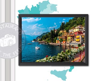 Peut inclure: Une photographie encadrée d'un village lacustre italien pittoresque. L'image présente des bâtiments colorés, des bateaux sur l'eau et des collines verdoyantes sous un ciel bleu clair. Le cadre est noir.