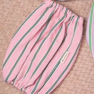 Puede incluir: Una manga de tela con abertura el&aacute;stica que presenta un patr&oacute;n de rayas finas rosas y blancas con rayas verticales de color verde oscuro. Una peque&ntilde;a etiqueta rectangular de tela blanca con el texto Coppy Paws est&aacute; cosida en el lateral.