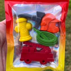 May include: A set of five colorful plastic toys in a clear plastic bag. The toys are shaped like a fire truck, a fire hydrant, a hose, a fireman's helmet, and an axe.