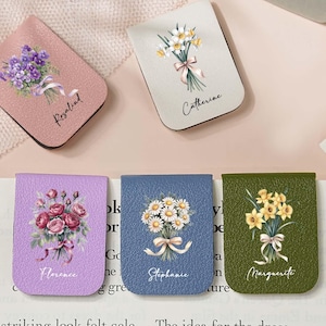 May include: A selection of floral magnetic bookmarks. Each bookmark displays a different flower bouquet design with names such as Rosalind, Catherine, Florence, Stephanie, and Marguerite. The bookmarks are in various colours, including pink, white, purple, blue, and green.