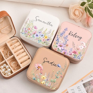 May include: An open brown leather jewelry box with gold jewelry, including necklaces, rings, and earrings. Three closed square jewelry boxes with floral designs and names: "Samantha", "Kelsey", and "Sadie".