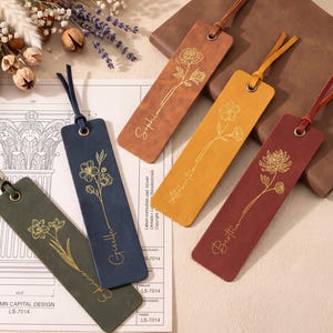 Può includere: Quattro segnalibri rettangolari in pelle nei colori verde oliva, blu navy, giallo senape e bordeaux. Ognuno presenta un disegno floreale a linee dorate, un nome personalizzato in corsivo, un occhiello in metallo e una nappa in pelle.