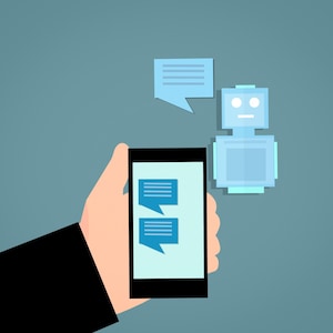 May include: An illustration of a hand holding a black smartphone with blue speech bubbles on the screen. A blue robot and speech bubble float nearby, suggesting a conversation or digital interaction. The background is a solid teal color.