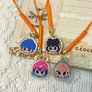Puede incluir: Cuatro colgantes de personajes de estilo anime con cordones naranjas. Cada colgante presenta un personaje diferente con ojos grandes y cabello colorido. Los colgantes están sujetos a cierres metálicos dorados. El fondo incluye un mapa vintage e ilustraciones de libélulas.