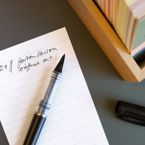 Rückseite einer schönetagebox-Karte. Ein Ereignis ist handschriftlich notiert: 2021 Gartensaison eröffnet mit … Ein Stift liegt parat, um den Text zu vervollständigen.