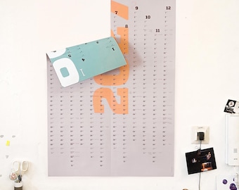 Könnte beinhalten: Ein vertikaler Wandkalender mit hellgrauem Hintergrund und großen pfirsichfarbenen Zahlen für das Jahr 2022. Die obere linke Ecke ist umgeklappt und gibt einen türkisfarbenen Bereich frei. Der Kalender zeigt Monate und Daten in schwarzer Schrift.