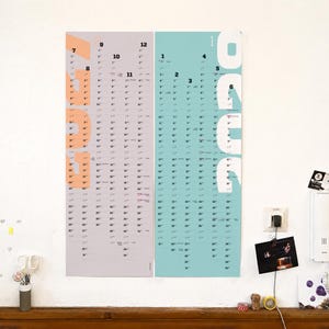 May include: A vertical wall calendar featuring two side-by-side panels. The left panel is light gray with large peach-colored text reading 2023. The right panel is light blue with large white text reading 2024. Both panels display monthly dates.
