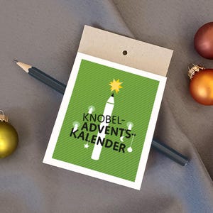Pode incluir: Um cartão verde com um lápis branco em forma de árvore de Natal. O texto no cartão diz "Knobel-Advents-Kalender".