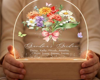 May include: An arched acrylic night light with a wooden base featuring a colourful watercolour bouquet of flowers, a pink ribbon, and butterflies. The text reads Grandma's Garden followed by the names Daisy, Kelly, Noah, Amelia, Olivia, Luna, James, Lucas.
