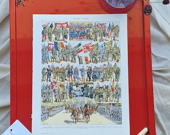 Pode incluir: Uma bandeja vermelha brilhante exibe uma impressão vintage intitulada "GRANDE GUERRE" retratando soldados e bandeiras. Uma etiqueta branca com um selo vermelho e uma caneta creme também estão presentes. Um pequeno vaso de vidro com flores secas também está presente.