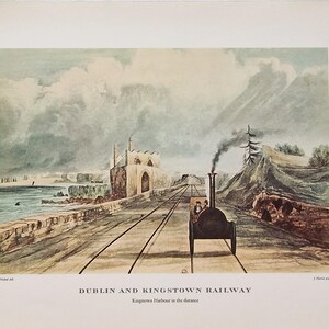 Può includere: Una stampa d'epoca della ferrovia Dublino e Kingstown, con un treno a vapore d'epoca che viaggia sui binari. L'opera raffigura una scena costiera con un muro di pietra, edifici e montagne sullo sfondo. Il testo "Dublin and Kingstown Railway" è in basso.
