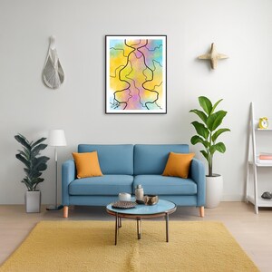 Può includere: Stampa artistica astratta in una cornice nera. L'opera presenta uno sfondo colorato con tonalità gialle, rosa e blu. Linee nere creano un design unico. La stampa è esposta sopra un divano blu con cuscini arancioni.