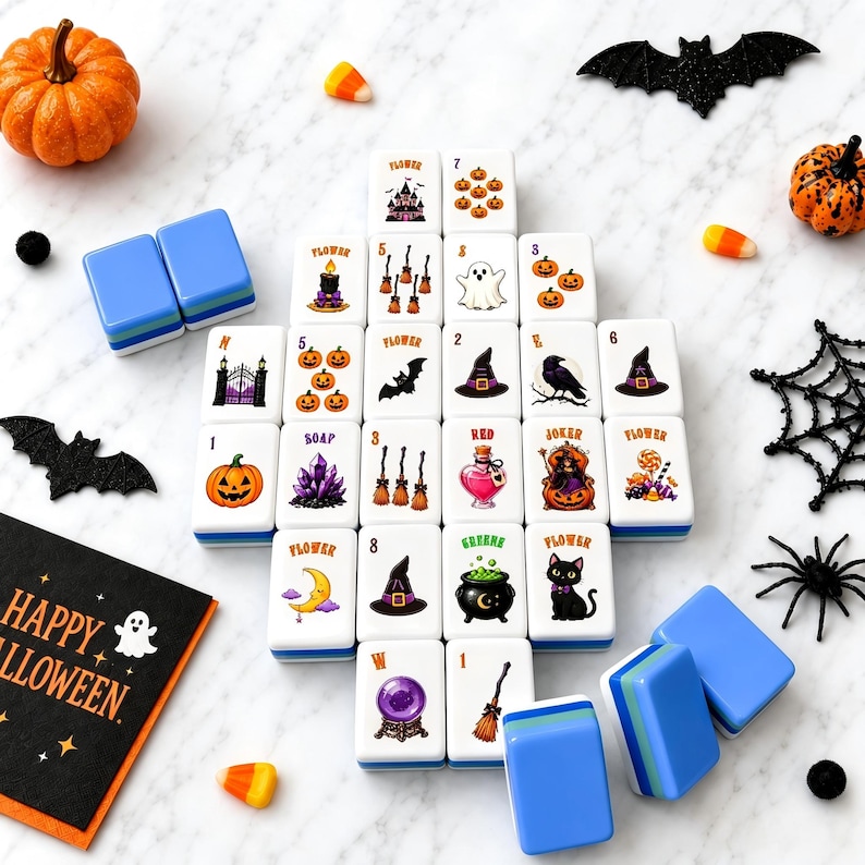 May include: A set of white mahjong tiles featuring colorful Halloween-themed illustrations including pumpkins, ghosts, bats, witches' hats, black cats, and cauldrons. The tiles are arranged in a grid alongside decorative plastic bats, spiders, and candy corn.