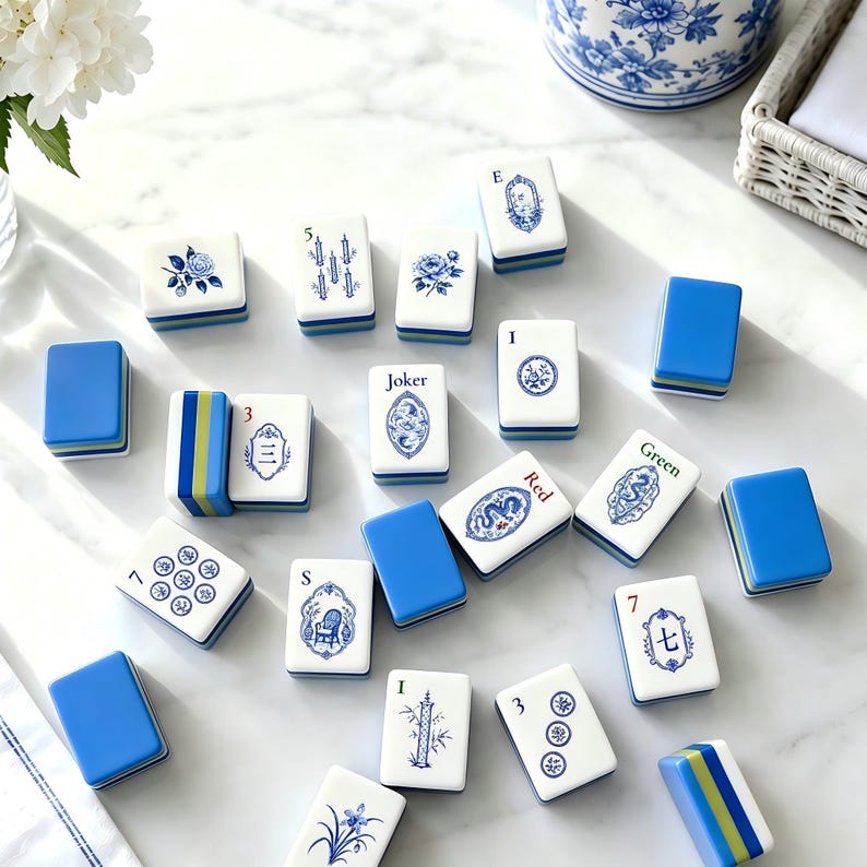 May include: A collection of rectangular Mahjong tiles featuring white faces with blue ink illustrations of flowers, bamboo, dragons, and text including Joker, Red, Green, 3, 5, 7, and S. The tiles have solid blue backs and layered blue and green edges.