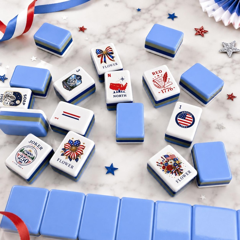 May include: A collection of rectangular mahjong tiles with light blue backs and white faces featuring patriotic American-themed graphics, including flowers, a map, the text 1776, and the word Joker, arranged on a white marble surface with star accents.