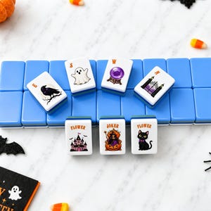 May include: A set of rectangular mahjong tiles with blue backs and white fronts featuring Halloween-themed illustrations including a ghost, a crystal ball, a raven, a gate, a haunted house, a witch in a pumpkin, and a black cat with text labels.