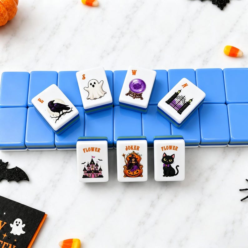 May include: A set of rectangular mahjong tiles with blue backs and white fronts featuring Halloween-themed illustrations including a ghost, a crystal ball, a raven, a gate, a haunted house, a witch in a pumpkin, and a black cat with text labels.