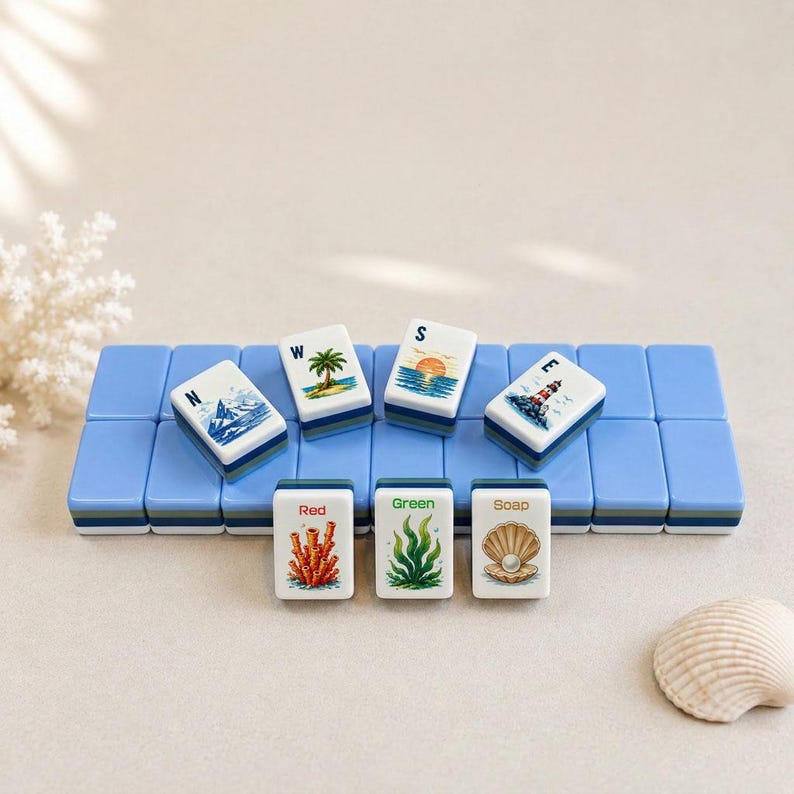 May include: A collection of white and blue Mahjong tiles featuring coastal imagery, such as a lighthouse, palm tree, and sunset. The tiles are displayed on a light blue rack, with additional tiles labelled "Red", "Green", and "Soap".