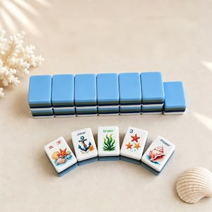 May include: A collection of blue and white Mahjong tiles with marine-themed designs. The tiles display images of starfish, seashells, and anchors. The set includes tiles with the words "Joker", "Green", and "Flower".