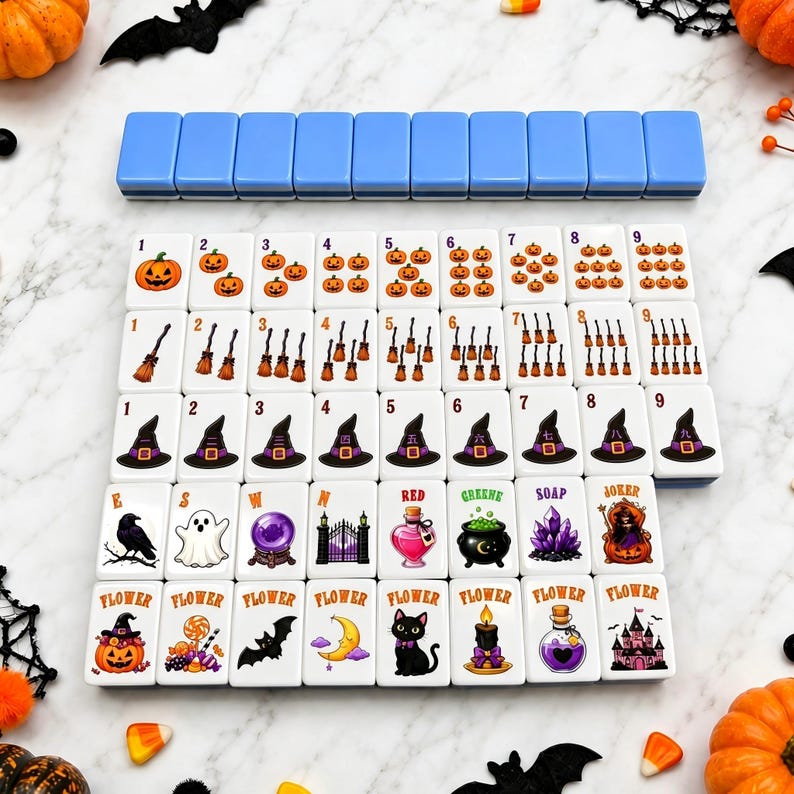 May include: A set of rectangular mahjong tiles featuring Halloween-themed illustrations including pumpkins, witch hats, brooms, ghosts, and black cats. The tiles are arranged in rows with numerical and thematic symbols, accompanied by a row of blue tiles.