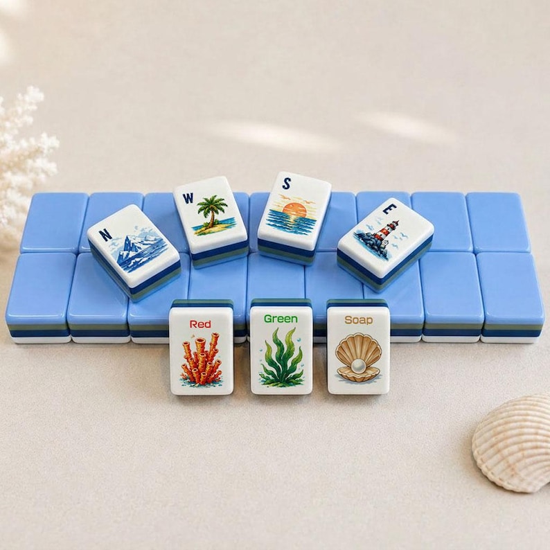 May include: A set of decorative Mahjong tiles with a coastal theme. The tiles feature images of a lighthouse, palm tree, sunset, and coral. The tiles are arranged on a blue base, with additional tiles displaying the words "Red", "Green", and "Soap".