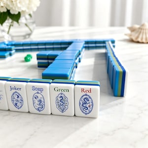 May include: A set of rectangular mahjong tiles with white faces and blue, green, and white layered sides. The front tiles feature blue and green ink illustrations of dragons within oval frames, with the text Joker, Soap, Green, and Red printed.