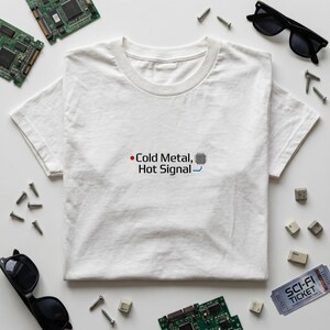 Peut inclure: T-shirt blanc avec l'inscription "Cold Metal, Hot Signal" en noir et bleu. Le motif comprend un circuit imprimé. L'image contient également des lunettes de soleil, des vis et des composants informatiques.