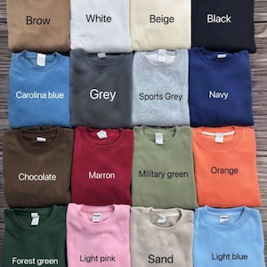 K&ouml;nnte beinhalten: Eine Auswahl an gefalteten Crewneck-Sweatshirts in verschiedenen Farben, darunter Braun, Wei&szlig;, Beige, Schwarz, Carolina-Blau, Grau, Sportgrau, Marine, Schokolade, Kastanienbraun, Milit&auml;rgr&uuml;n, Orange, Waldgr&uuml;n, Hellrosa, Sand und Hellblau. Jedes Sweatshirt hat ein Etikett.