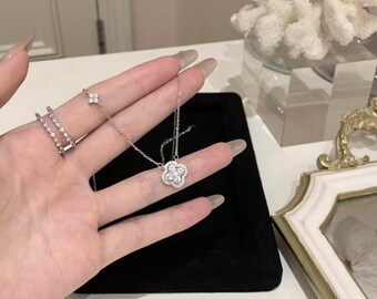 May include: A silver necklace with a clover-shaped pendant, adorned with sparkling gemstones. A matching ring with a clover design and a delicate ring with multiple small gemstones are also visible. The jewelry is displayed on a black surface.