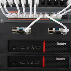 May include: A stack of black computer servers with white network cables connected. The servers have the "ThinkCentre" logo and a red stripe. The top server has a network switch with multiple ports.