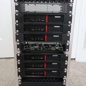 May include: A silver computer server rack with multiple black ThinkCentre computer units. Each unit has a red stripe and various ports. The rack also includes a top panel with network ports and a bottom shelf.