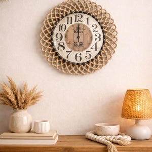 Puede incluir: Un reloj de pared redondo con un borde de cuerda tejida. La esfera del reloj tiene números y manecillas negras, con el texto "KILLY" y "EST. 2002 Loc. 2017". El reloj está montado en una pared blanca sobre una mesa de madera.