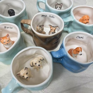 以下が含まれることがあります： 様々な色のセラミックマグのコレクションで、それぞれの中に小さな動物の置物が入っています。「Junior」、「Carl」、「Benji Sadie」などの名前が書かれたマグもあります。マグカップはコーヒーや紅茶に最適です。