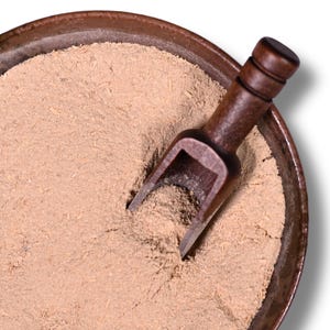 May include: A close-up shot of a brown ceramic bowl filled with a light brown powder. A small, dark wooden scoop rests inside the bowl, partially submerged in the powder. The bowl has a dark rim and a textured surface.