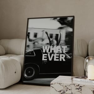 May include: A monochrome framed print featuring the word "WHATEVER" in white. The image depicts a person with raised arms in a car. The print is propped against a cream sofa, beside a marble coffee table, creating a modern interior scene.