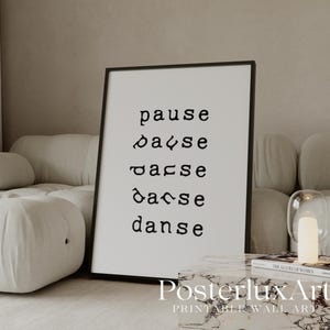 May include: A black framed print featuring the words "pause, danse, danse, danse, danse" in a modern font. The print is displayed in a neutral-toned living room setting, next to a white sofa and a marble-topped table.