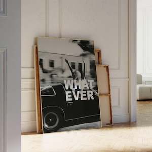 May include: Monochrome framed print showing a person with arms raised from a classic car, with the word "WHATEVER" in white. The artwork is propped against a wall, alongside other framed canvases.