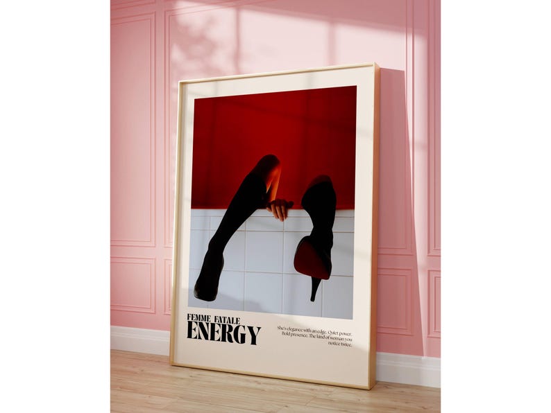 May include: Framed art print featuring a red and white abstract design with black silhouettes of legs and high heels. The text "FEMME FATALE ENERGY" is displayed in bold, black font. The artwork is displayed in a room with pink walls.