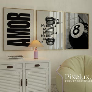 May include: Three framed wall art prints. The first says "AMOR" in large black letters. The second features lips and the word "bla". The third shows a black and white eight ball. The prints are in gold frames.